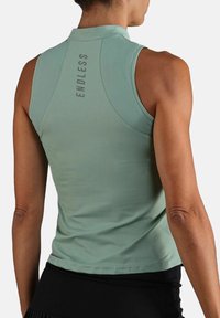 Lichtgroene mouwloze sporttop met een hoge kraag, een gebogen zoom en "ENDLESS" in een reflecterende afwerking op de achterkant.