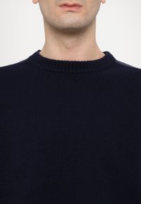 Pull en maille bleu marine avec un col rond côtelé et une texture lisse, ne présentant aucun logo ni motif visible.