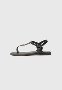 Sandalia de cuero negro con suela plana, que presenta un diseño de tirante en T, hebilla ajustable en el tobillo y acentos minimalistas.