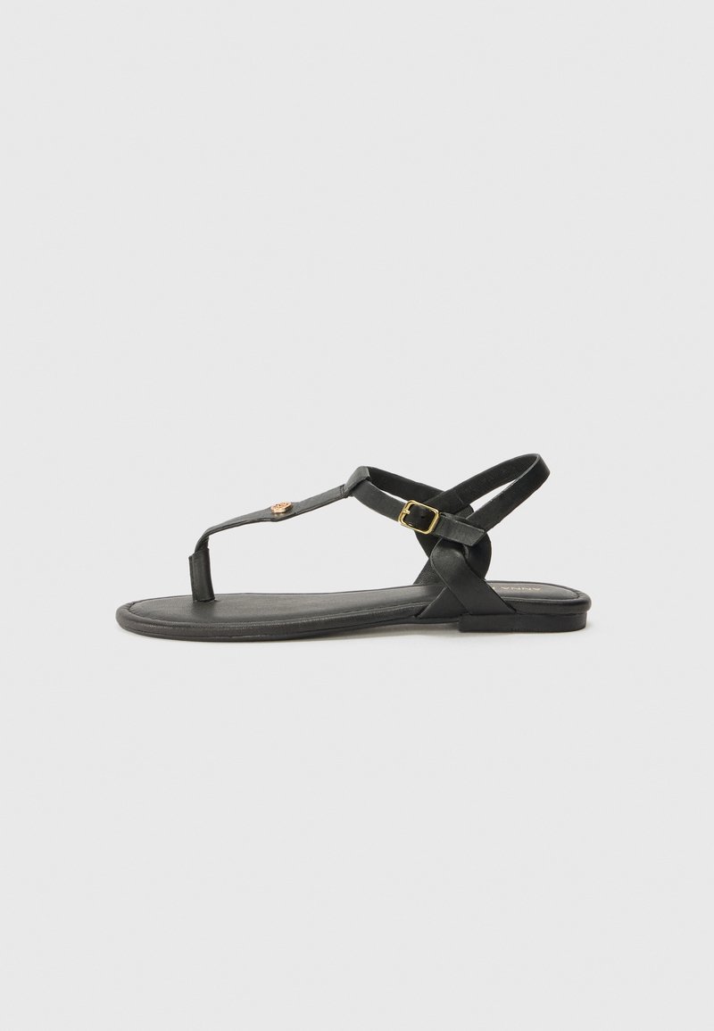 Black leather sandal with a flat sole, featuring a T-strap design, adjustable ankle buckle, and minimalistic accents.