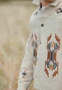 Beige overhemd met knopen, voorzien van ingewikkelde multiculturele geometrische borduursels. Opvallende patronen op de borst en mouwen, met een gestructureerde stof.