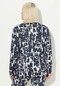 Giacca a fantasia bianco e nero con un design astratto, maniche lunghe e una vestibilità rilassata, realizzata in un tessuto morbido ed elastico.
