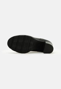 Suela de zapato negra con un diseño plano, hecha de goma. Presenta un patrón texturizado con surcos y crestas para mayor agarre.