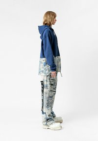 Sudadera navy con un panel inferior texturizado de un azul más claro; pantalones sueltos con patrón; botas rechonchas de color blanco roto; diseño y silueta minimalistas.
