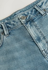 Lyseblå denimjeans med en falmet finish, udstyret med lukning med metalknap og tanfarvet syning langs sømmene.