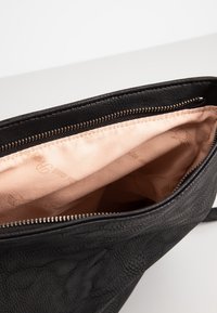 Borsa nera in pelle con esterno liscio, chiusura con cerniera e fodera interna in raso rosa chiaro con sottili motivi di marchio.