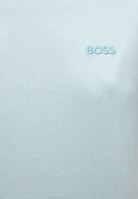 Ανοιχτό μπλε ύφασμα με τη λέξη «BOSS» κεντημένη με κλωστή σε αντίστοιχη μπλε απόχρωση στην επάνω δεξιά πλευρά.