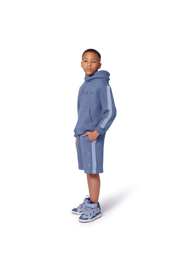 Blauwe katoenen hoodie en short set met logodetail, voorzien van een kangoeroezak en gestreepte zijkanten. Gepaard met blauwe en witte sneakers.