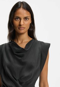 Schwarze, ärmellose Bluse mit weich fallendem Stoff. Ausgestattet mit einem Wasserfallausschnitt und strukturierten Schulternähten für eine lockere Passform.