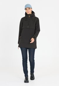 Svart, huva pullover med framdragkedja, stor framficka och oranga dragkedjeaccenter. Bärs med mörka jeans och svarta stövlar.