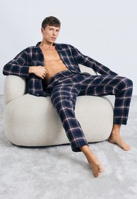 Camisa de cuadros en tonos navy con botones y pantalones a juego sobre una figura sentada, con una textura suave y un ajuste relajado, en un fondo claro.
