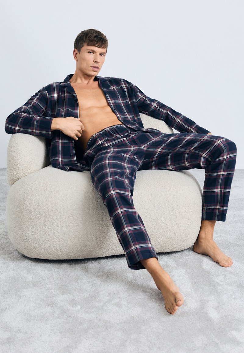 Camisa de cuadros en tonos navy con botones y pantalones a juego sobre una figura sentada, con una textura suave y un ajuste relajado, en un fondo claro.