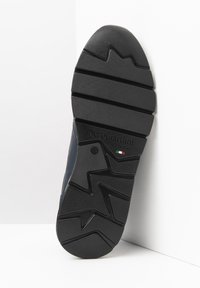 Semelle de chaussure en caoutchouc noir avec un motif de bande de roulement en zigzag, logo en relief, et détail du drapeau italien ; fabriquée à partir de matériaux durables pour une traction et un confort optimaux.