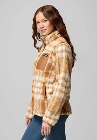 Fuzzy, plaid fleece jacket in tan and cream with a high collar and brown chest pocket, featuring a zip closure and soft texture.