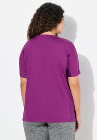 Paarse T-shirt met korte mouwen van een soepele, lichte stof. Beschikt over een relaxte pasvorm en een lichte kromming aan de zoom. Gepaard met grijze sportbroeken.