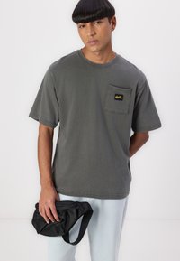 Gray cotton t-shirt with a round neckline and short sleeves; features a left chest pocket with a black and yellow logo.