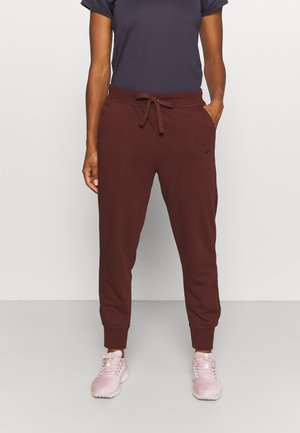 Personne portant un pantalon de jogging rouge foncé avec taille à cordon et chevilles resserrées, associé à des chaussures de sport rose clair et un haut sombre.