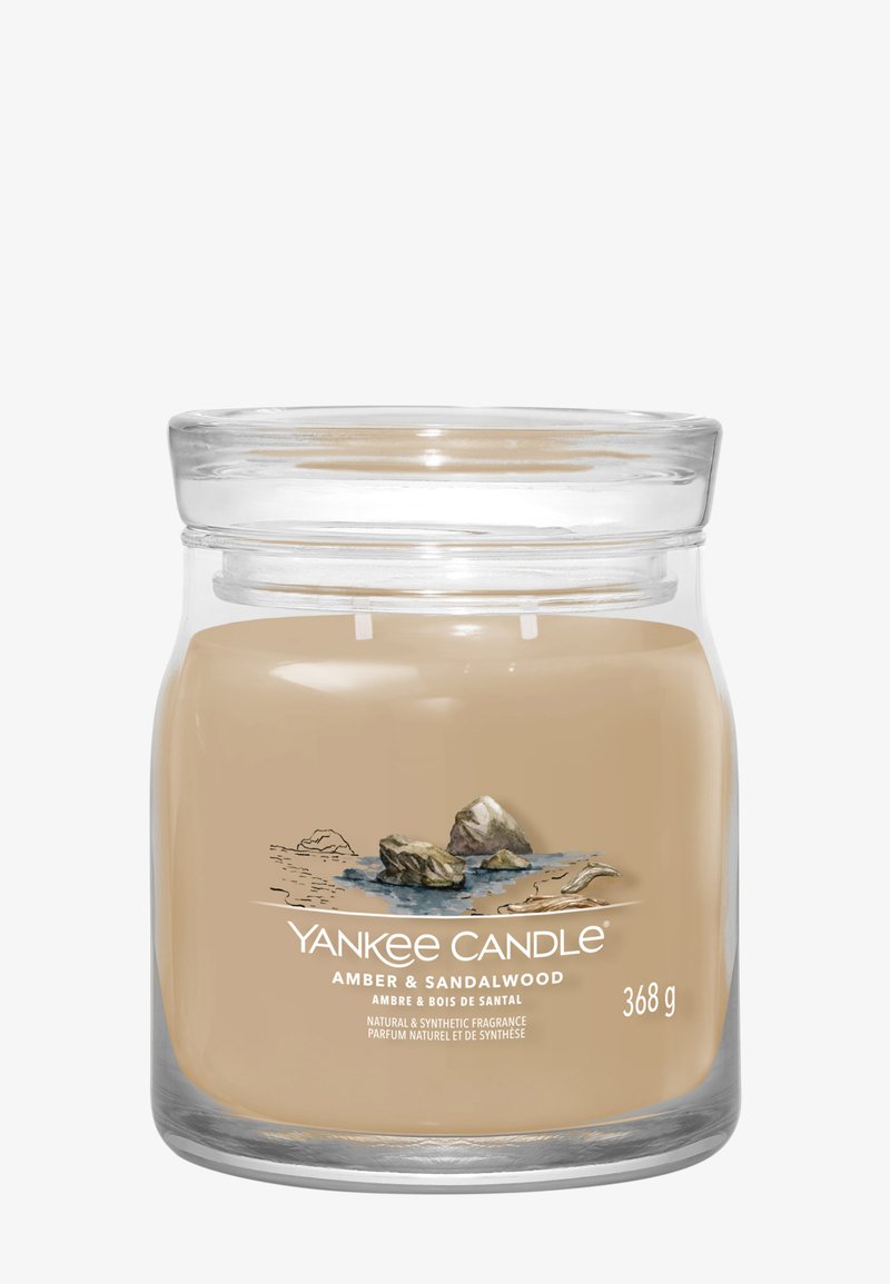 Bougie Yankee Candle en pot avec cire beige Ambre & Bois de santal, deux mèches, et étiquette représentant des rochers au bord de l'eau, pesant 368 g.