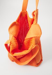 Geantă de umăr împletită, de culoare portocalie vibrantă, cu un material texturat și două mânere, având un design deschis în partea de sus și un interior spatios.