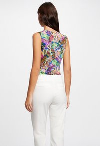 Top sin mangas con un vibrante patrón de hojas tropicales en múltiples colores, combinado con pantalones blancos a medida.