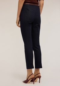 Pantalons en denim bleu marine avec une silhouette ajustée et une coupe jusqu'aux chevilles. Présente une texture lisse et un détail de poche arrière. Associés à des chaussures à talons bourgogne.