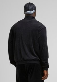 Jachetă pulover din velur negru, cu guler înalt, croială lejeră și manșete ribbate. Textură netedă și talie elastică pentru confort.
