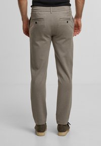 Lichtbruine op maat gemaakte broek van zachte stof. Beschikt over twee achterzakken met knopen en een slim fit ontwerp.