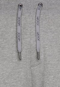 Graue Jogginghosen aus weichem Material, mit geripptem Gummibund und flachen Kordeln mit Markenenden. Verfügt über eine Seitennaht-Tasche.