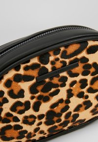 Väskan i leopardmönster har en mjuk, texturerad yta; den har en svart läderkanter och en dragkedjestängning. Accentuerad med en subtil logoplåt.