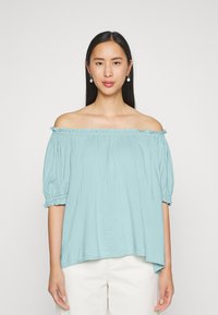 Blusa azul clara off-the-shoulder com mangas bufantes, decote franzido e um caimento solto. Feita de tecido macio, com a parte de trás mais longa.