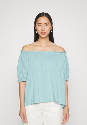 Blusa azul clara off-the-shoulder com mangas bufantes, decote franzido e um caimento solto. Feita de tecido macio, com a parte de trás mais longa.