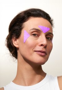 Des taches triangulaires violettes placées sur le front au-dessus des yeux, avec une peau lisse visible en dessous et un débardeur blanc en arrière-plan.