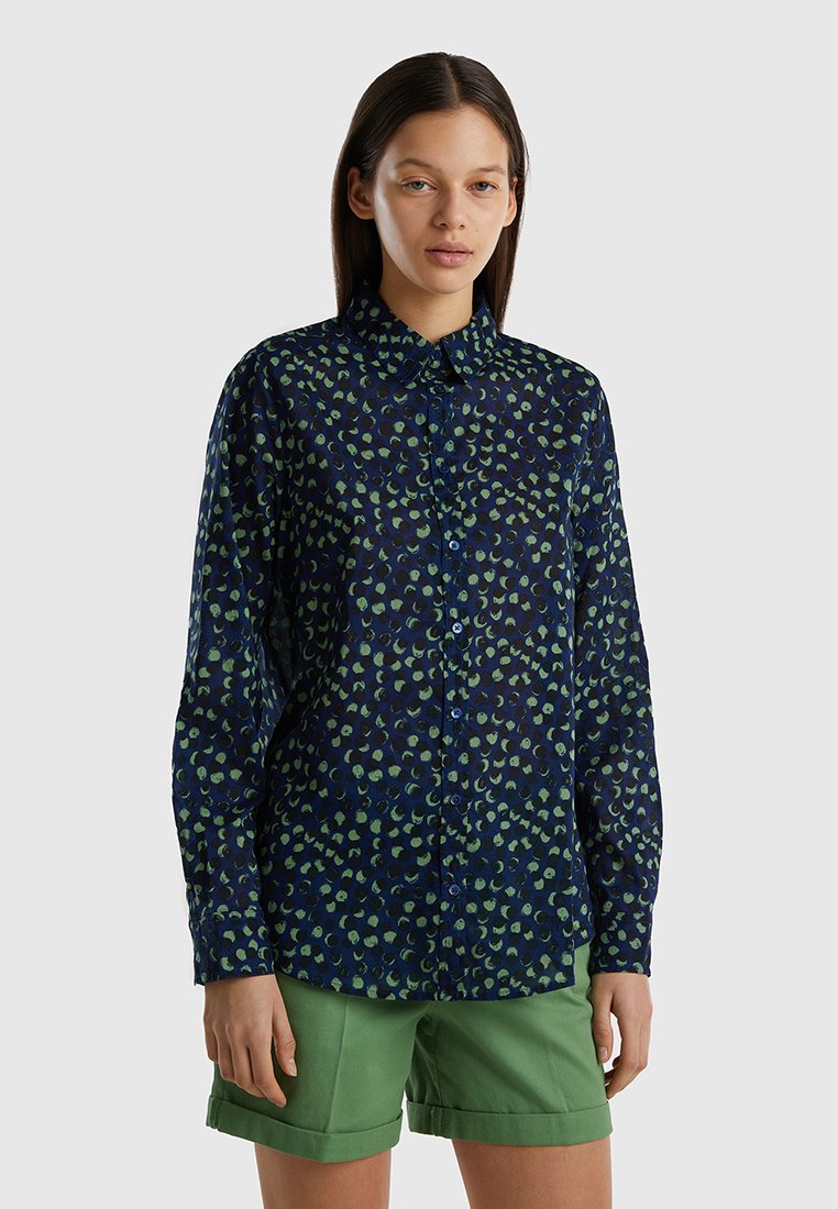 Camicia blu navy con motivo a foglie verdi, maniche lunghe e colletto a punta, abbinata a pantaloni corti verdi. Tessuto con una texture liscia.