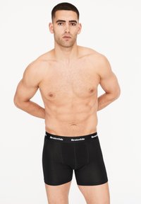Černé boxerky z měkké tkaniny s širokým pasem, na kterém je bílým písmem uvedeno jméno značky "Resteröd", a těsným střihem.