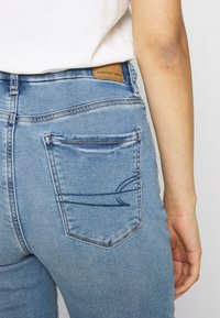Los jeans de mezclilla azul cuentan con un bolsillo trasero con un sutil diseño de costura. La cinturilla muestra una etiqueta de cuero marcada con 'American Eagle'.