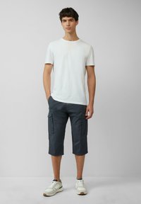 White crew-neck t-shirt, dark gray knee-length cargo shorts with side pockets, and white sneakers with gray accents. Smooth fabric texture.
