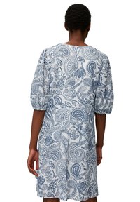Valkoinen mekko, jossa on sinisiä paisley-kuvioita, lyhyet puffihihat ja pyöreä pääntie. Kankaan pinta on sileä ja siinä on yksityiskohtaisia kukkakuoseja.