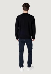 Maglione nero a trama con colletto rotondo, abbinato a jeans blu scuro e sneaker bianche, visto da dietro.