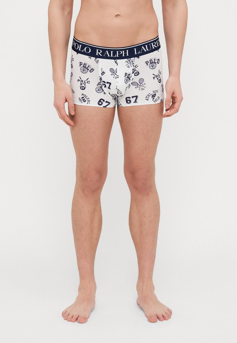 Valkoiset boxerit tummansinisellä vyötäröllä, jossa on teksti "POLO RALPH LAUREN." Kankaan pinnassa on toistuva painatus logoista ja numeroista tummansinisinä.