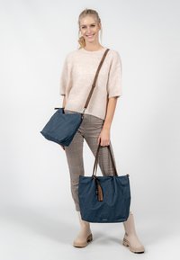 Navy blue textile bags with brown straps; one is a small crossbody, the other a larger tote with a tassel detail on the zipper.