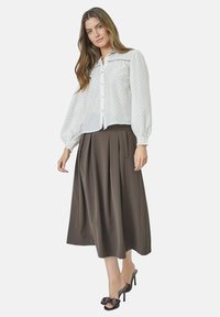 White blouse with dotted pattern and button closure, paired with a long, pleated brown skirt and black open-toe shoes with bow detail.