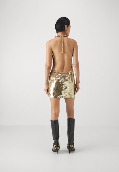 Kuldse sädelusega mini kleit madala selja ja kaelakaelakee detailiga, kombineeritud mustade läikivate kuni põlve saapadega ja pannalaksendiga.