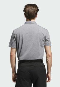 Szara koszulka polo z krótkim rękawem, teksturowanym wzorem i kołnierzykiem, zestawiona z ciemnymi spodniami. Widok od tyłu ukazuje przeszycia i dopasowanie.