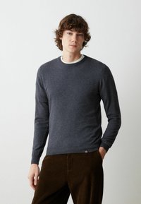Maglione grigio scuro lavorato a maglia con maniche lunghe e scollo rotondo, caratterizzato da un orlo a costine e un piccolo logo sul lato sinistro in basso.
