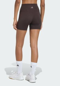 Hnedé šortky s vysokým pásom, hladkou textúrou a prešívanými detailmi. V kombinácii s bielou športovou obuvou a ponožkami s čiernymi pásikmi.