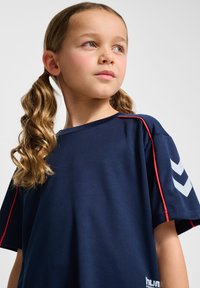 Marinblått sportt-shirt med korta ärmar, med en röd accent på axeln och en grå chevrondesign på ärmen.