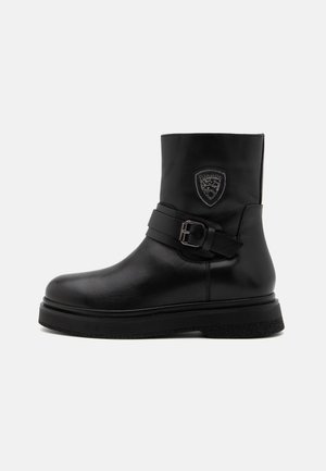 Zwarte leren enkelboot met een ronde neus, een chunky zool, een brede riem met een gesp en een decoratieve schildpatch aan de zijkant.