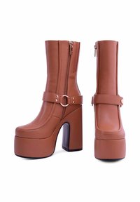 Stivali platform in ecopelle marrone con tacco a blocco, zip laterale e una fascia con dettaglio della fibbia circolare. Texture liscia e forma strutturata.