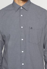 Svartvit rutmönstrad skjorta med knappar och krage, med en framficka och vita knappar, tillverkad av ett lätt tyg.