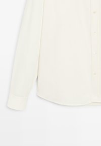 Camicia button-up crema, maniche lunghe, tessuto liscio, orlo curvo, piccoli bottoni, colletto standard, senza motivi o dettagli visibili.